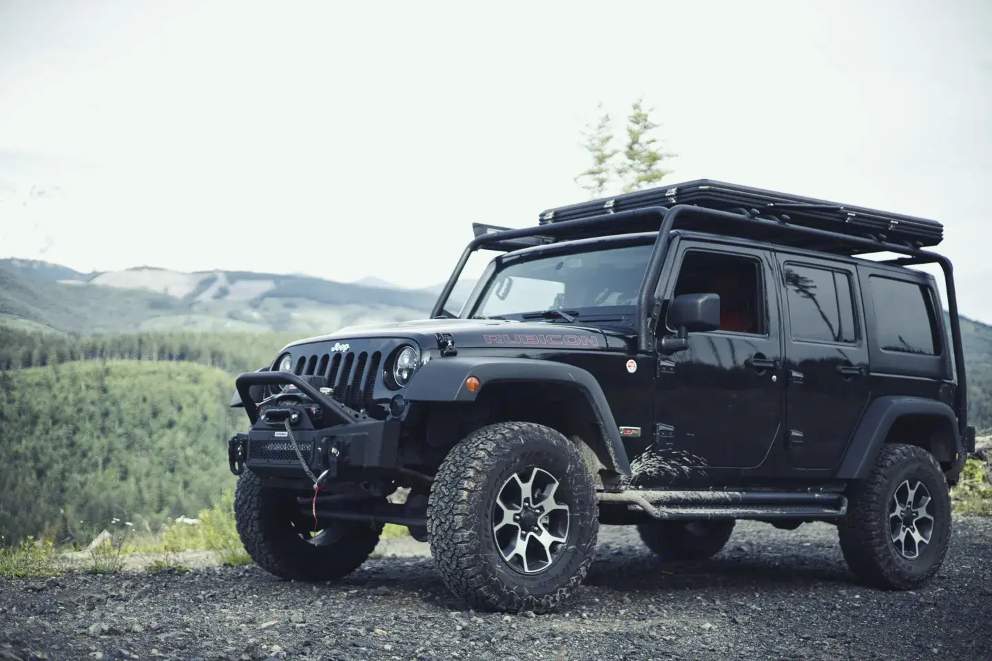Black Jeep Rubicon parked at a mountain overlook above a forested valley