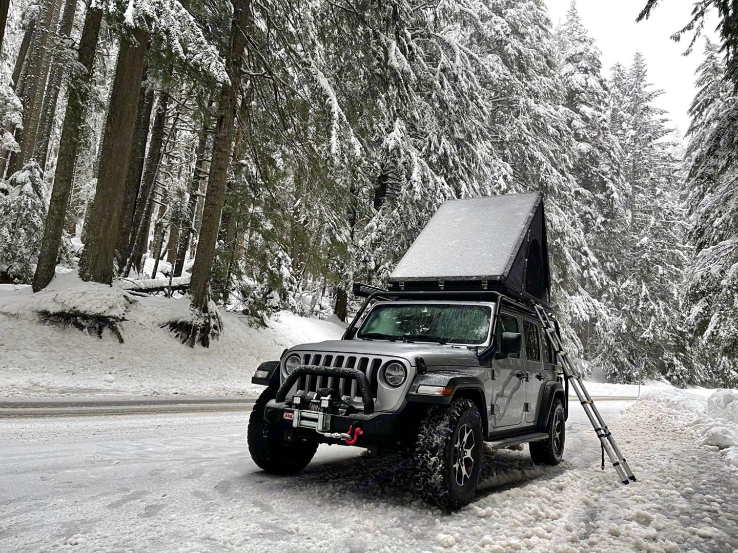 Jeep Wrangler with rooftop tent deployed on a snow-covered forest road