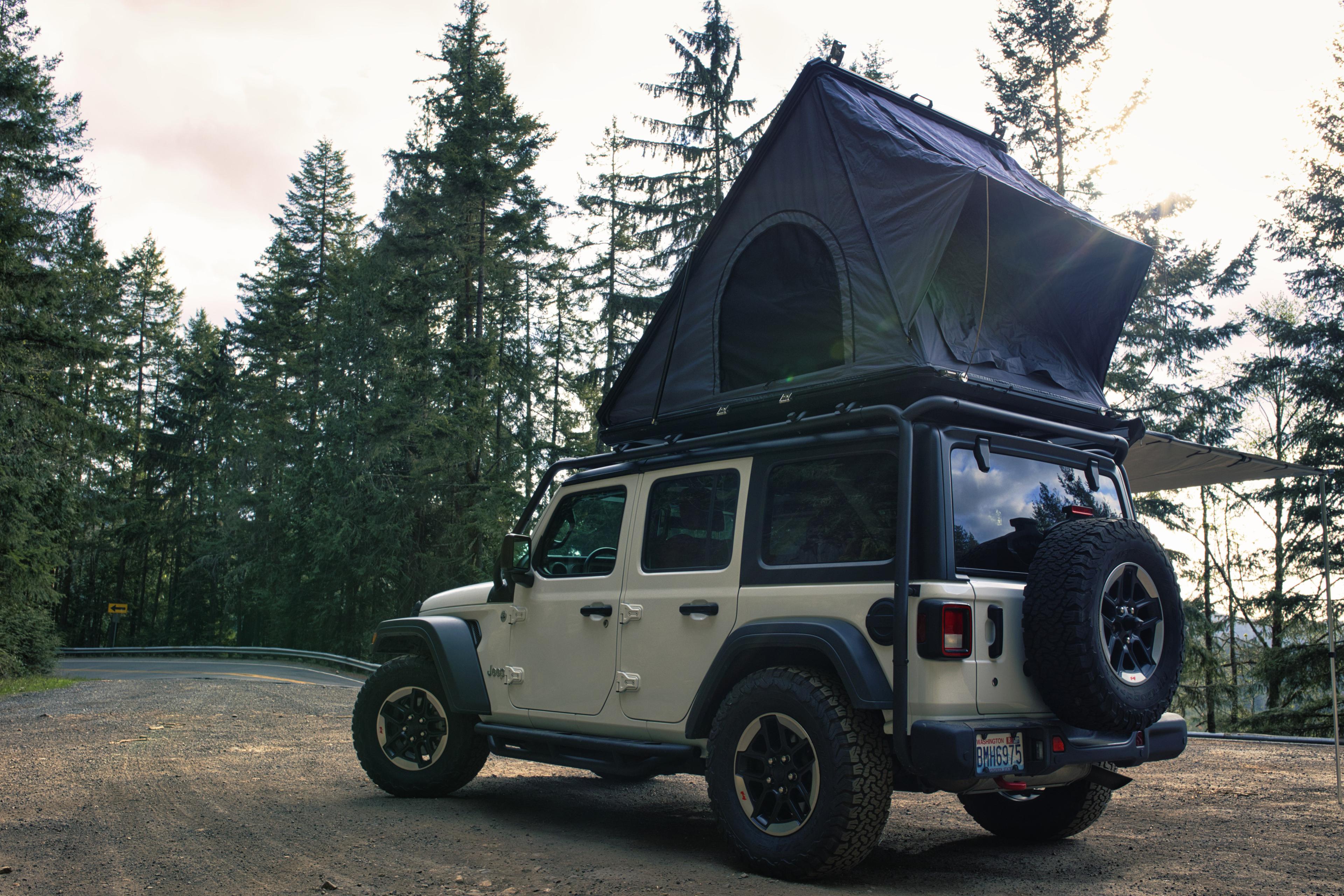 Hardshell rooftop tent opened on a Jeep's roof rack in old-growth forest