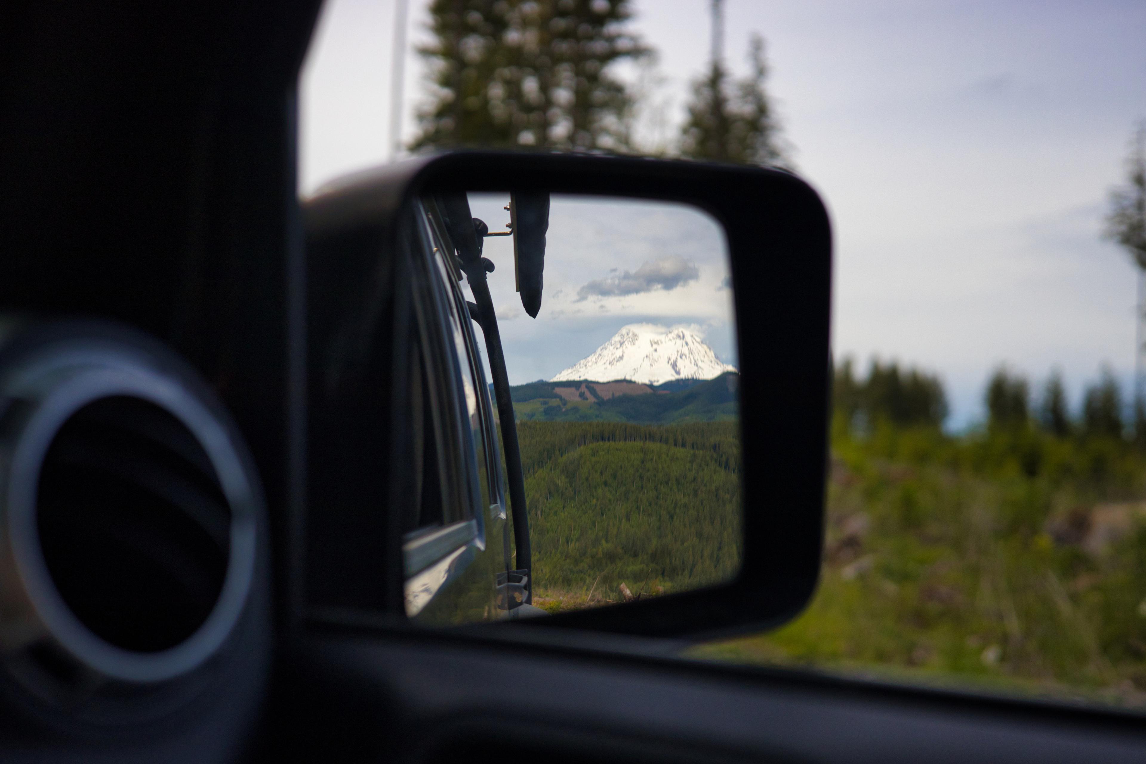 Mount Rainier's snowy peak framed in a Jeep's side mirror, above miles of forest